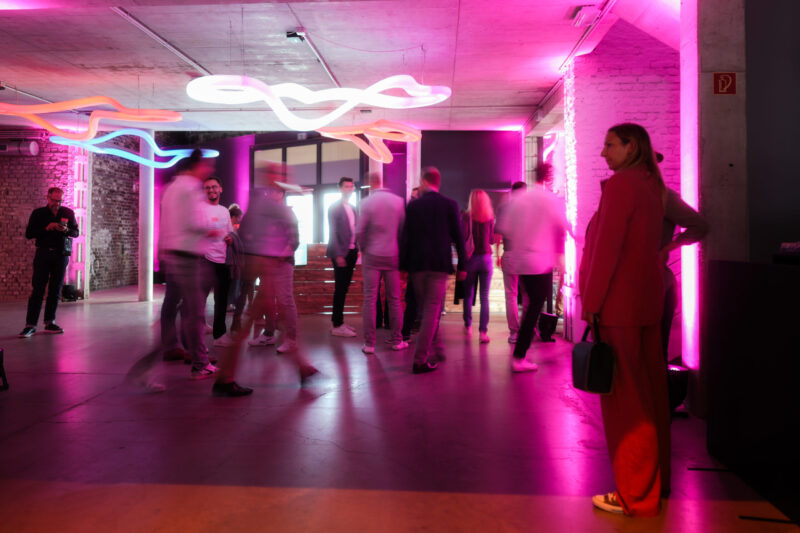 Die Abbildung zeigt eine Menschenmenge in einer Halle mit Neonlichtern.